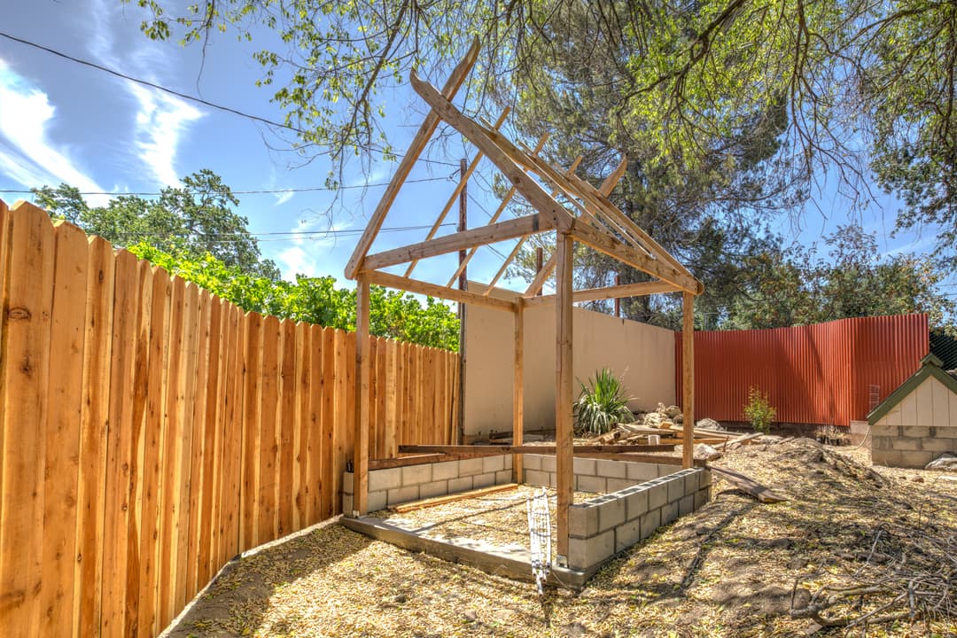 Wooden frame shed under construction in a backyard with a wooden fence