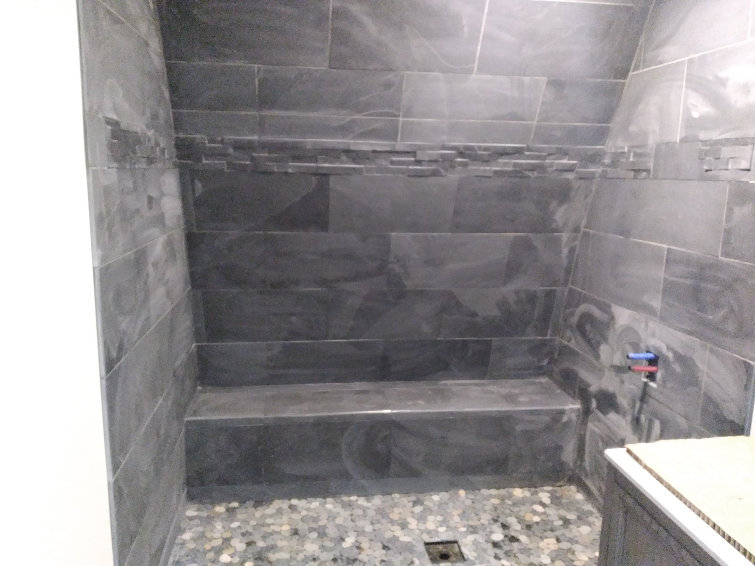 Modern shower with black tiles, built-in bench, and pebble floor