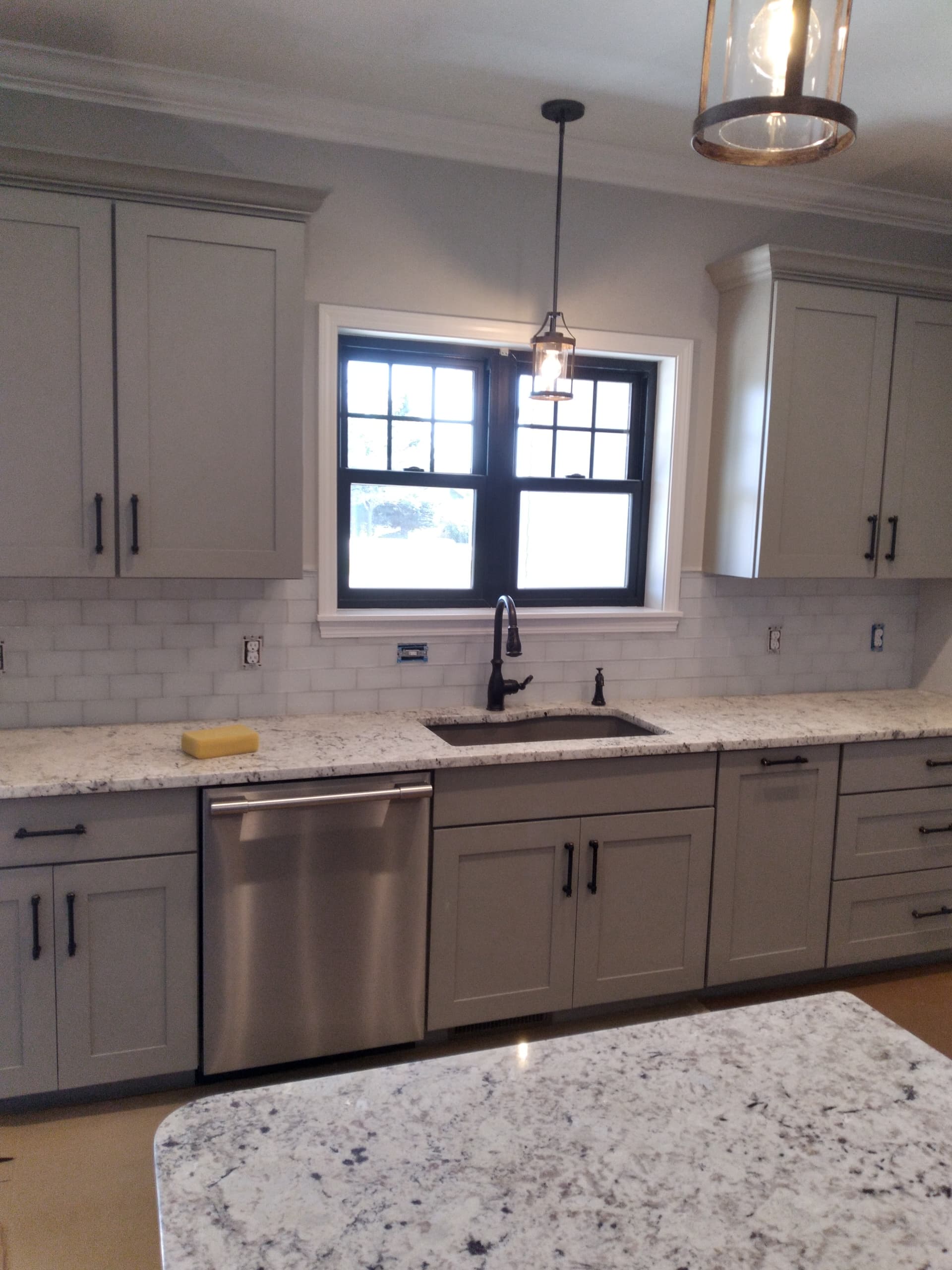 Modern kitchen with grey cabinets, white granite countertops, stainless dishwasher, and pendant lights