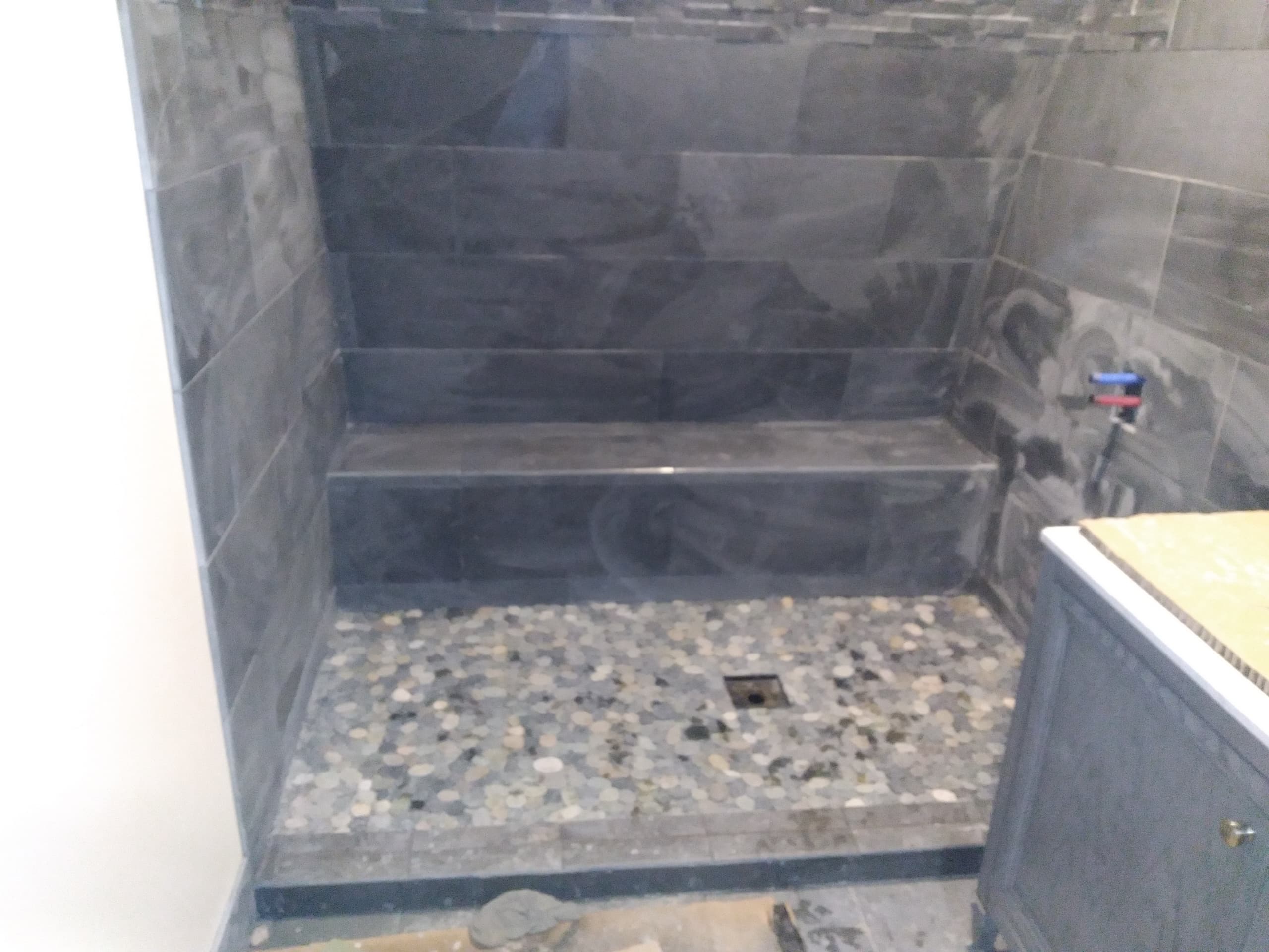 Tiled shower with bench and pebble stone floor under construction