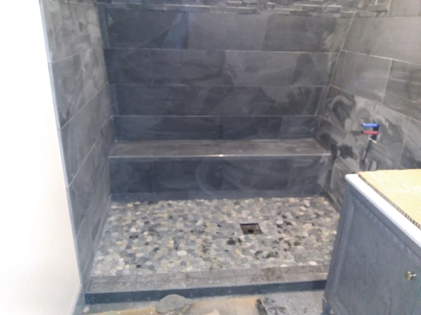 Tiled shower with bench and pebble stone floor under construction