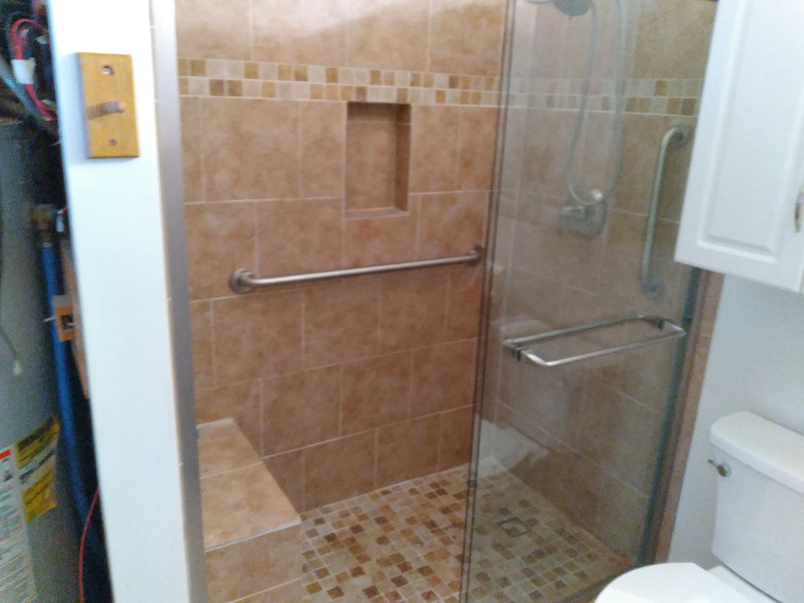 Modern walk-in shower with tan tiles, glass door, bench, and grab bars