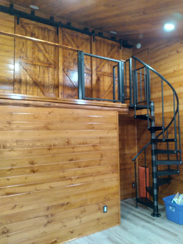 Wooden loft with spiral staircase and sliding barn doors inside a cozy cabin room